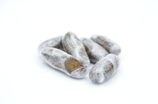 Plusieurs olivettes de hasch soigneusement emballées dans un film plastique transparent, dont l’une est partiellement ouverte, exposant son intérieur brun foncé et compact.