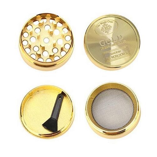 Grinder en métal doré démonté en quatre parties : couvercle gravé, compartiment de broyage perforé, tamis pour filtrer les particules fines et récupérateur avec une mini spatule.